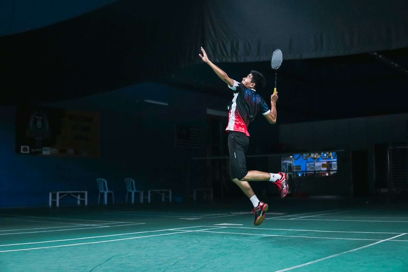 A badminton player jumping to hit a shuttlecock on an indoor court.