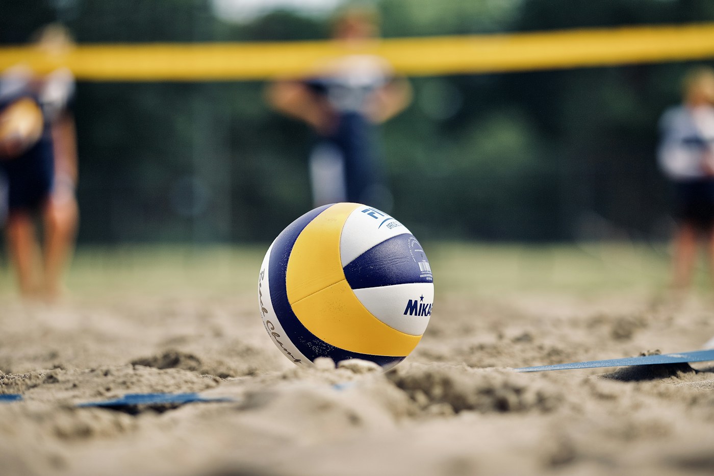 A volleyball on the sand beside a beach court.