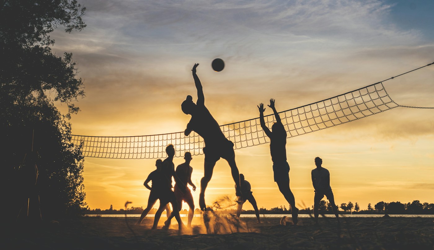 Friends playing volleyball across a net at sunset.